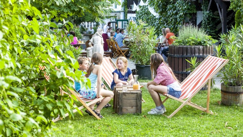 Kinder sitzen auf Liegestühlen im Garten eines Cafés.