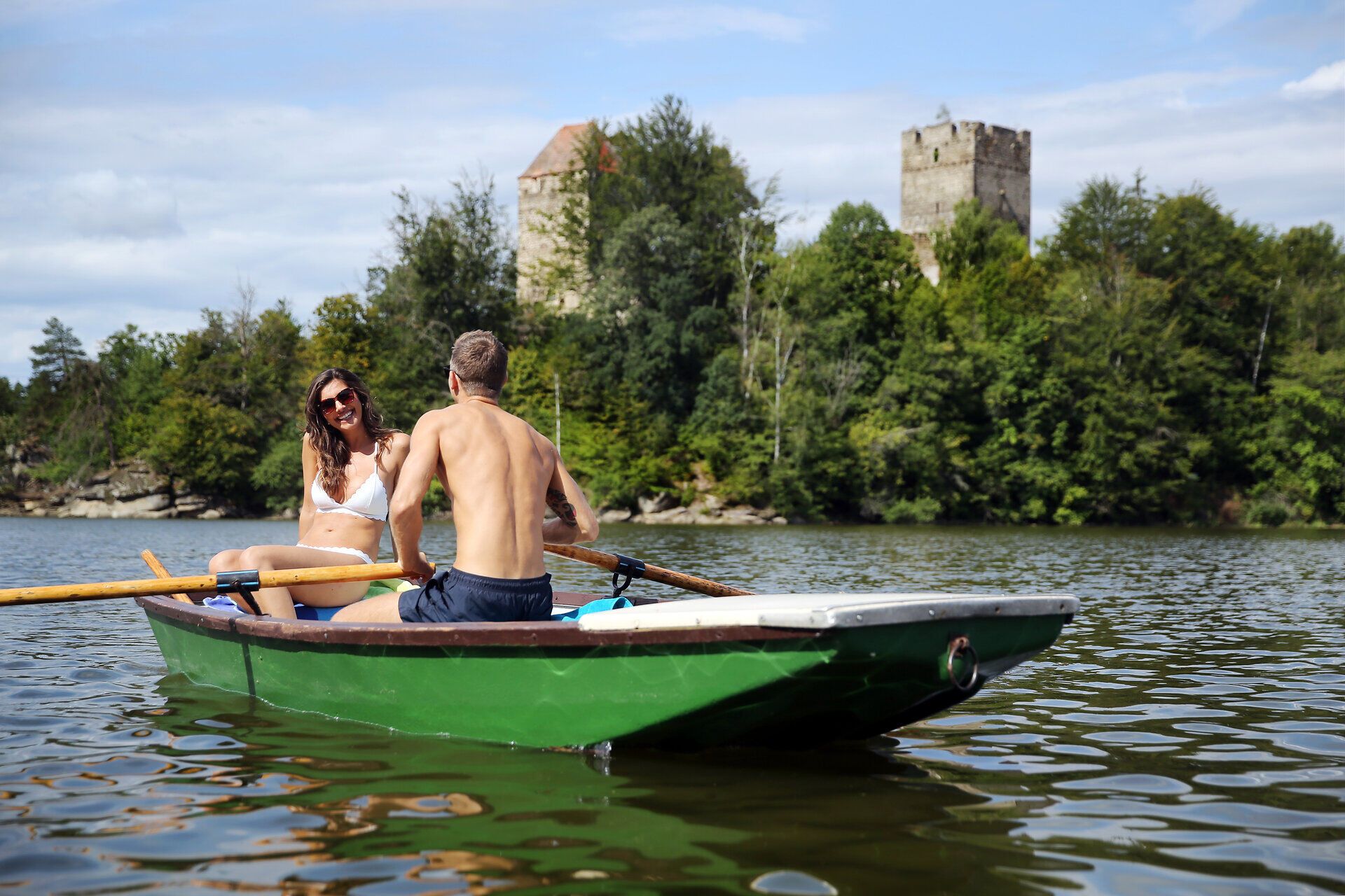 Ein sonniger Tag am Stausee Ottenstein lädt zu einer romantischen Bootsfahrt ein. Die sanften Wellen spiegeln die umliegenden Wälder und die majestätischen Ruinen wider, während das Lachen der beiden Ausflügler die friedliche Atmosphäre erfüllt.