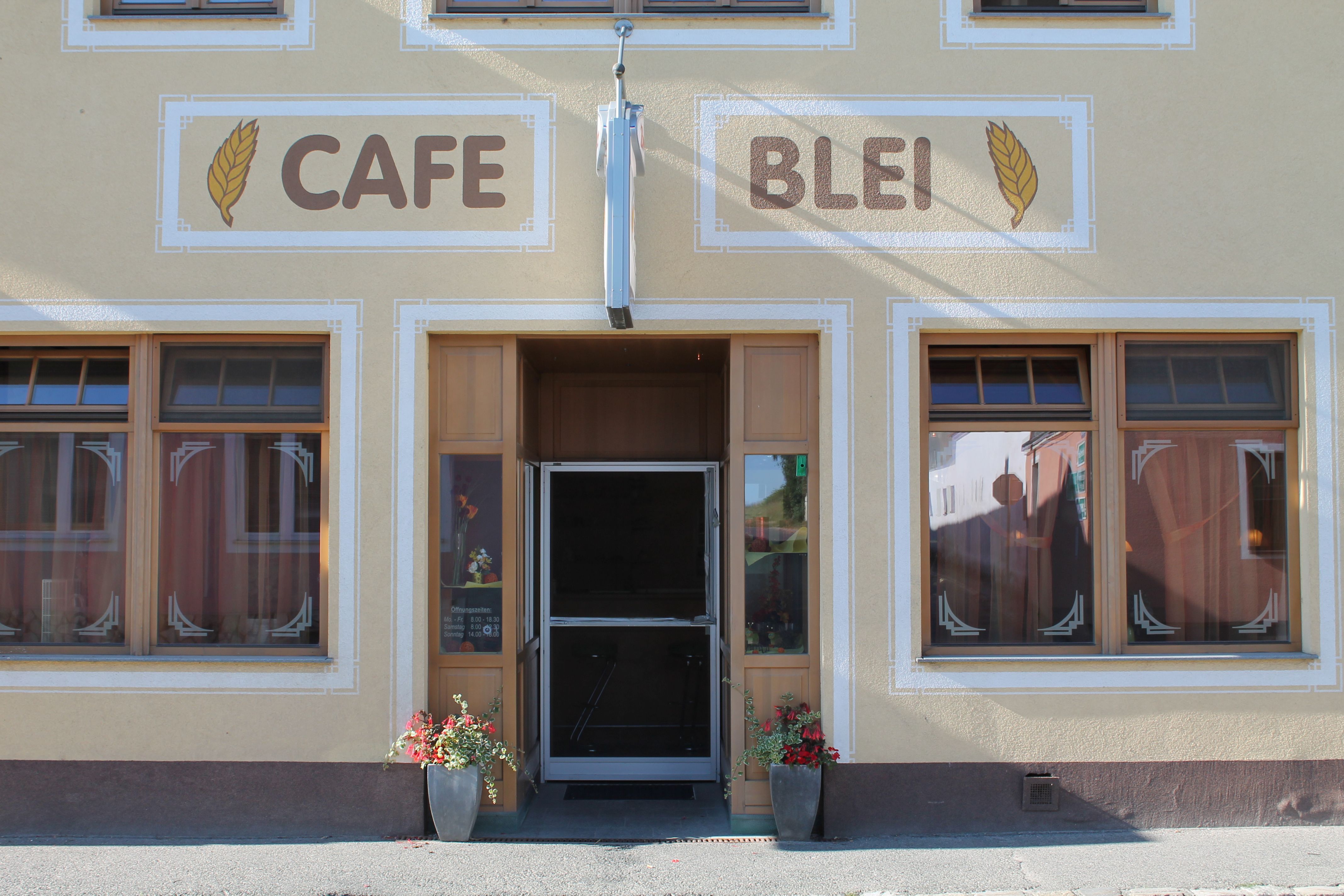 Eingang eines Cafés mit der Aufschrift 'Cafe Blei' und Blumendekoration.
