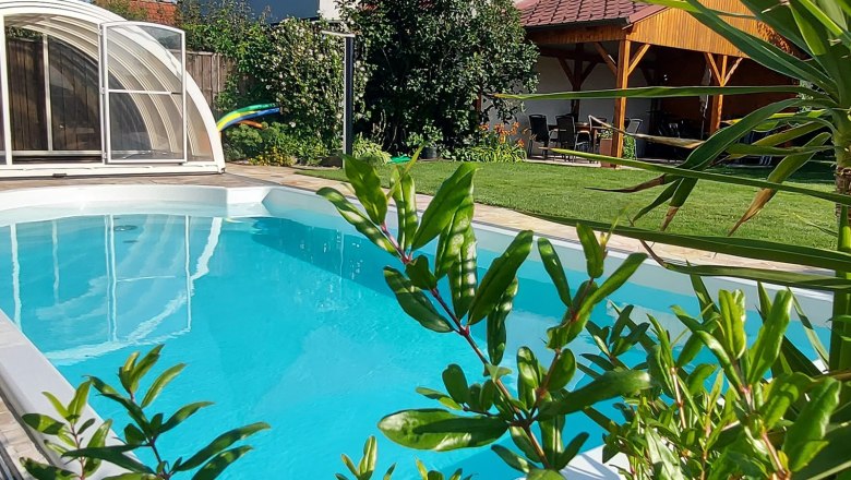 Ein privater Garten mit einem Pool, umgeben von Pflanzen und einem &uuml;berdachten Sitzbereich.