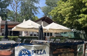 Gastgarten mit Blick auf das Gebäude der Pizzeria, im Hintergrund Bäume.