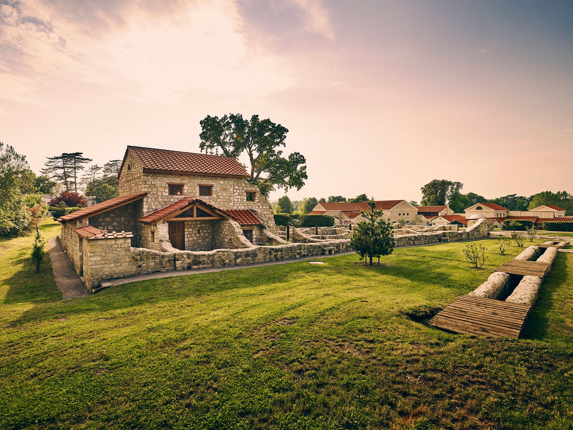 Römerstadt Carnuntum mit rekonstruierten Gebäuden und roten Dächern, umgeben von grünen Bäumen und Rasenflächen.