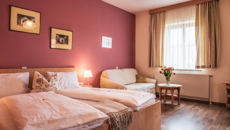 Gemütliches Gästezimmer mit Doppelbett, Sofa, Tisch und Blumenstrauß.