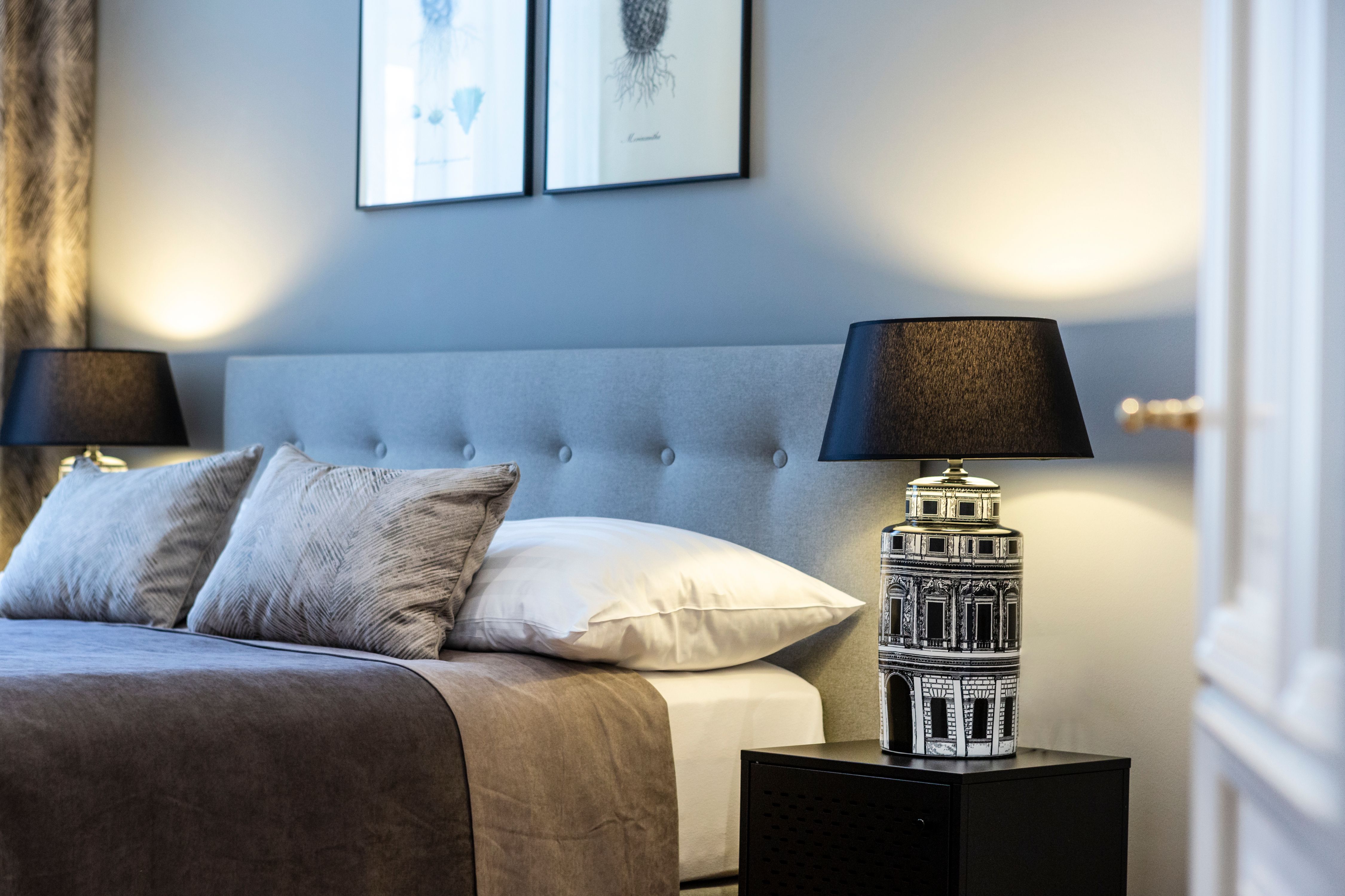 Elegantes Doppelzimmer mit grauem Kopfteil, zwei Kissen, Nachttischlampe und Wandbildern.