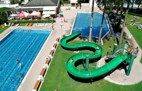 Luftaufnahme eines Freibads mit zwei Becken und einer grünen Wasserrutsche.