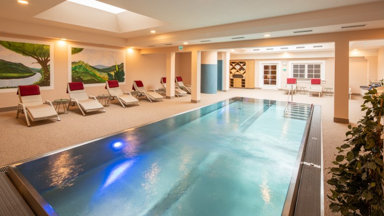 Ein moderner Indoorpool im Hotel-Spa mit Liegestühlen und Wandmalereien