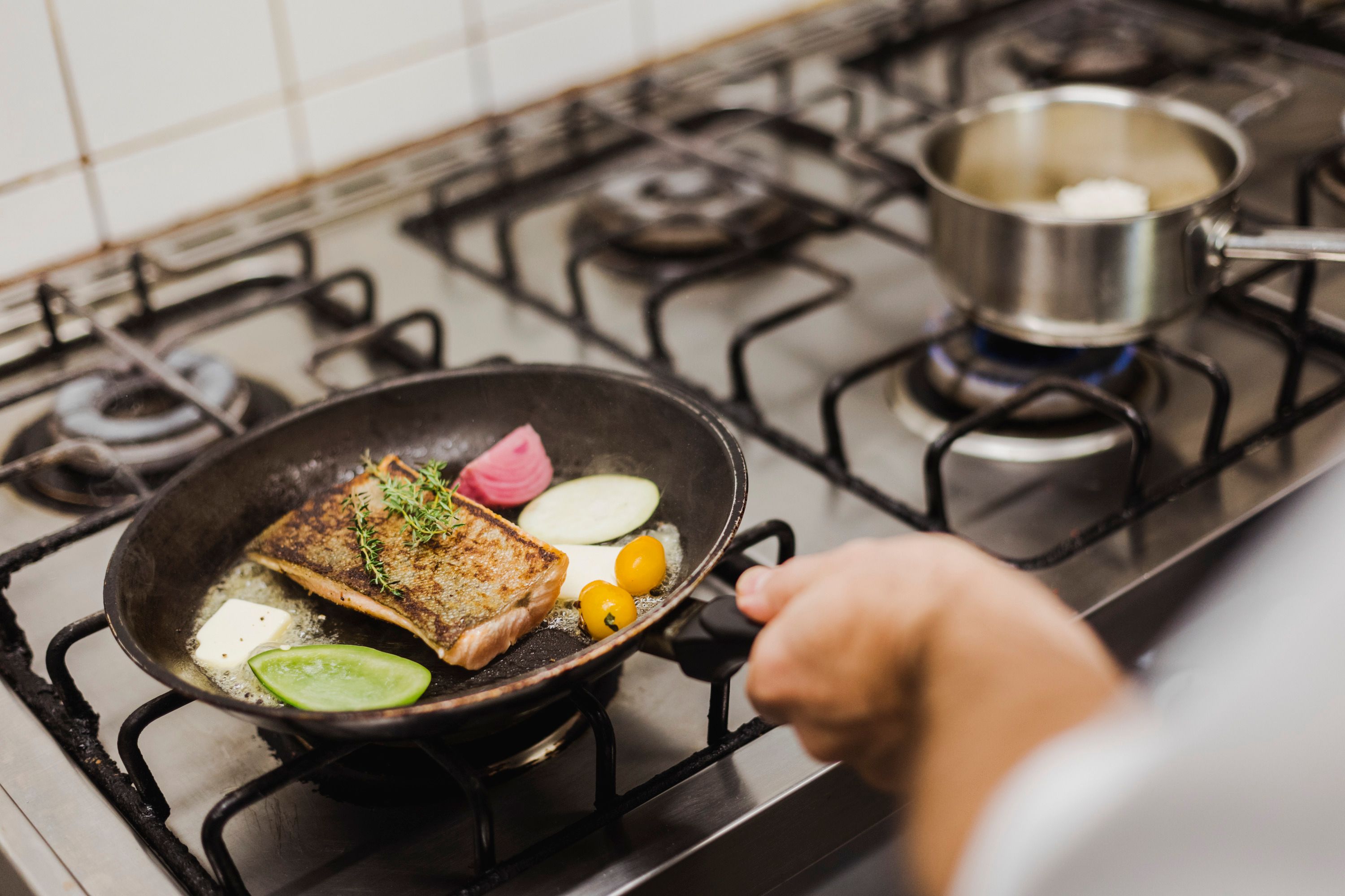 Eine Pfanne mit Fisch, Gemüse und Kräutern auf einem Herd.