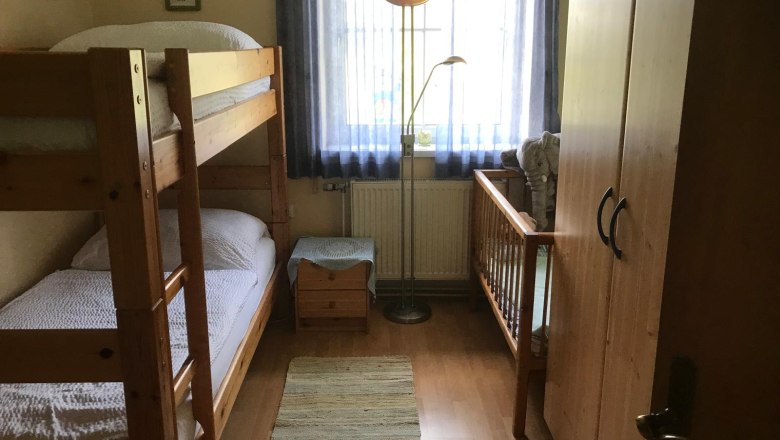 Kinderzimmer mit Etagenbett, Kinderbett, Schrank und Stehlampe.