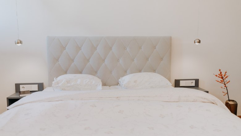 Ein elegantes Schlafzimmer mit einem gro&szlig;en Bett, zwei Nachttischen und einer Vase mit roten Beeren.