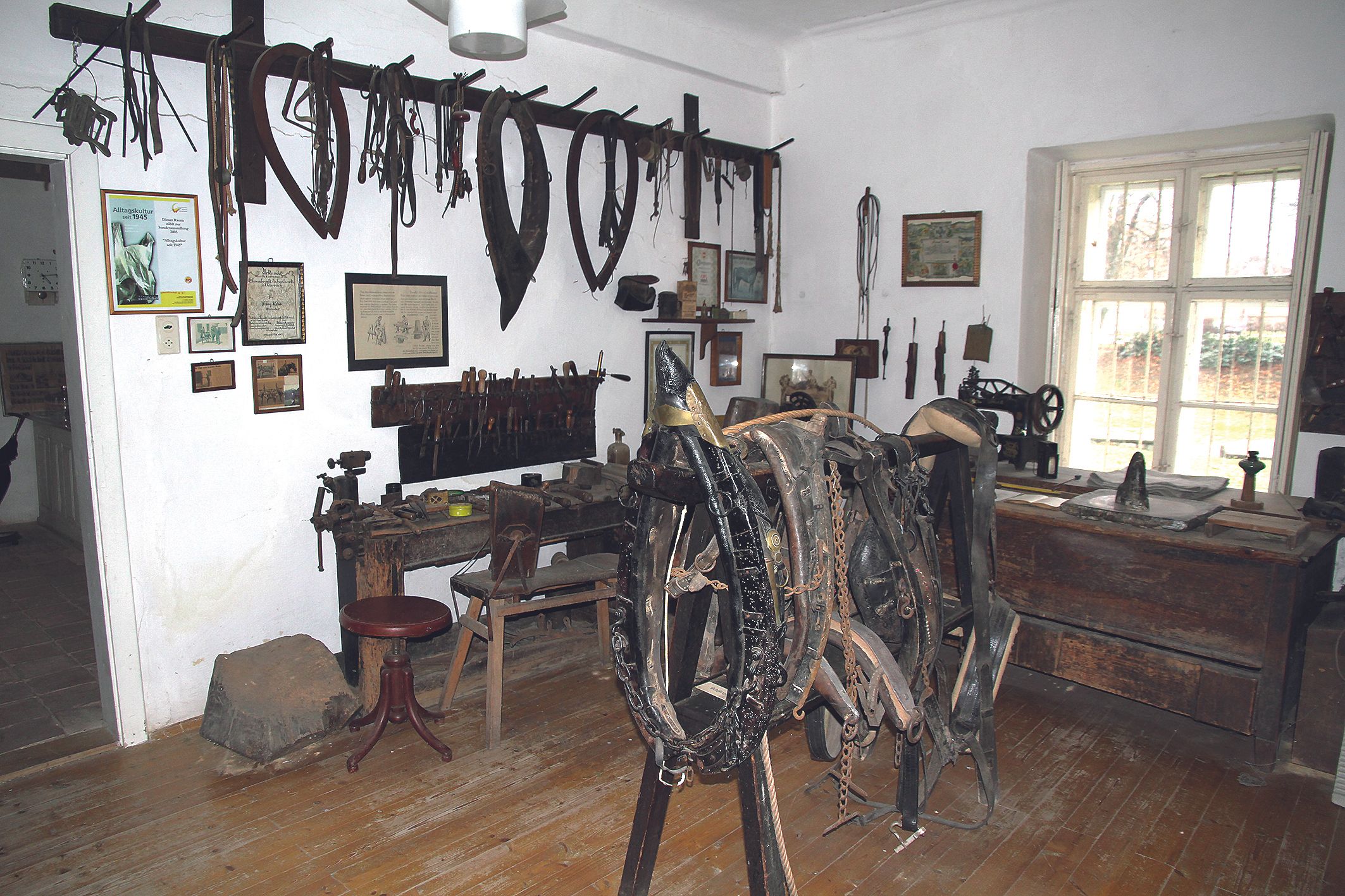 Ein Raum in einem Heimatmuseum mit alten Werkzeugen und Pferdegeschirr an den Wänden.