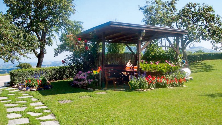 Ein Pavillon auf einem gr&uuml;nen Rasen mit bunten Blumen und B&auml;umen im Hintergrund.
