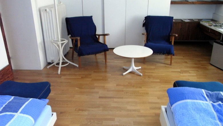 Linke Gert, Mag., © Mag. Linke Ein Zimmer mit zwei blauen Sesseln, einem weißen runden Tisch und zwei Betten mit blauer Bettwäsche auf Holzboden.