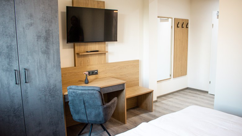 Modern eingerichtetes Hotelzimmer mit Schreibtisch, Fernseher, Kleiderschrank und Spiegel.