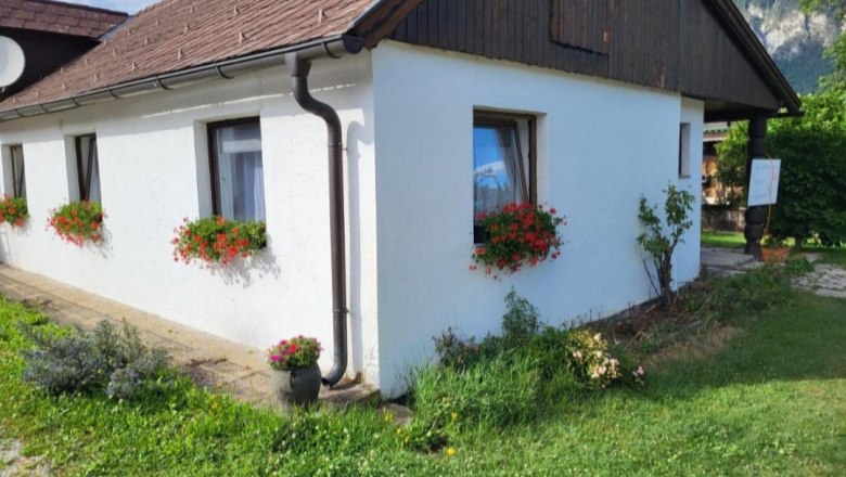 Wei&szlig;es Haus mit roten Blumen in Blumenk&auml;sten vor den Fenstern, gr&uuml;ne Wiese im Vordergrund.