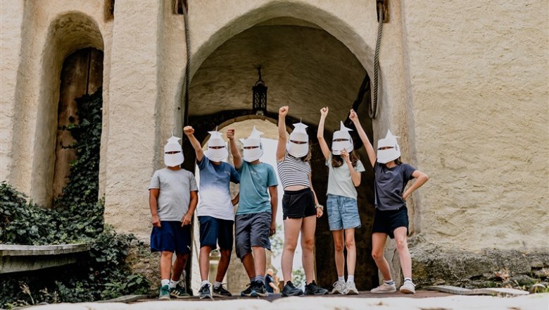 Gruppe von Menschen mit Papierhelmen vor einem Burgtor.