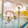 Seniorengruppe bei Wassergymnastik im Hallenbad mit Schwimmnudeln.