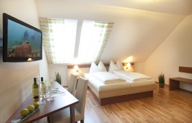 Ein gem&uuml;tliches G&auml;stezimmer mit Doppelbett, Flachbildfernseher, Tisch mit St&uuml;hlen und Dachfenstern.