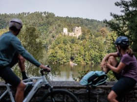 Die sanften Hügel um den Stausee Dobra laden zu einer entspannenden Pause ein. Radfahrer genießen die malerische Aussicht auf die beeindruckende Ruine, während die Natur in voller Blüte steht und die sanften Wellen des Wassers leise plätschern.