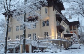 Ein großes, elegantes Hotel im Winter, umgeben von schneebedeckten Bäumen und einem verschneiten Auto.