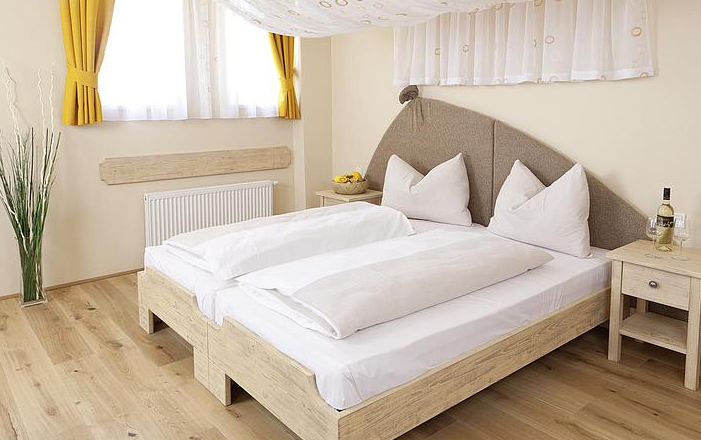 Ein gem&uuml;tliches G&auml;stezimmer mit Doppelbett, gelben Vorh&auml;ngen und Holzm&ouml;beln.