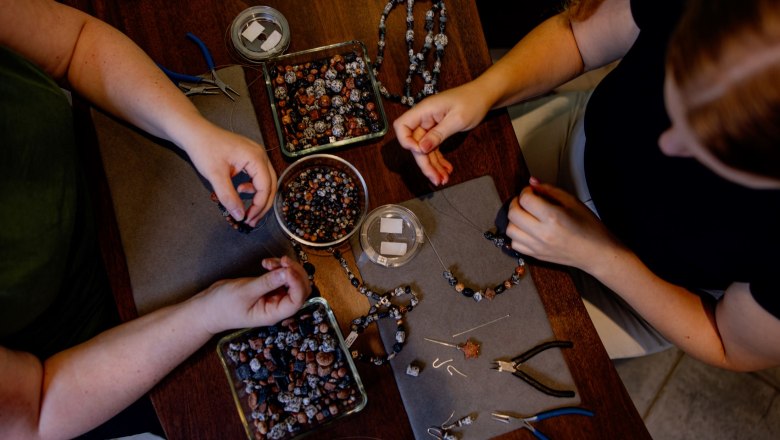 Zwei Personen fertigen Granitschmuck an einem Tisch mit Perlen und Werkzeugen.