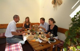 Vier Personen sitzen an einem Tisch in einem gemütlichen Innenhof und genießen eine Mahlzeit.