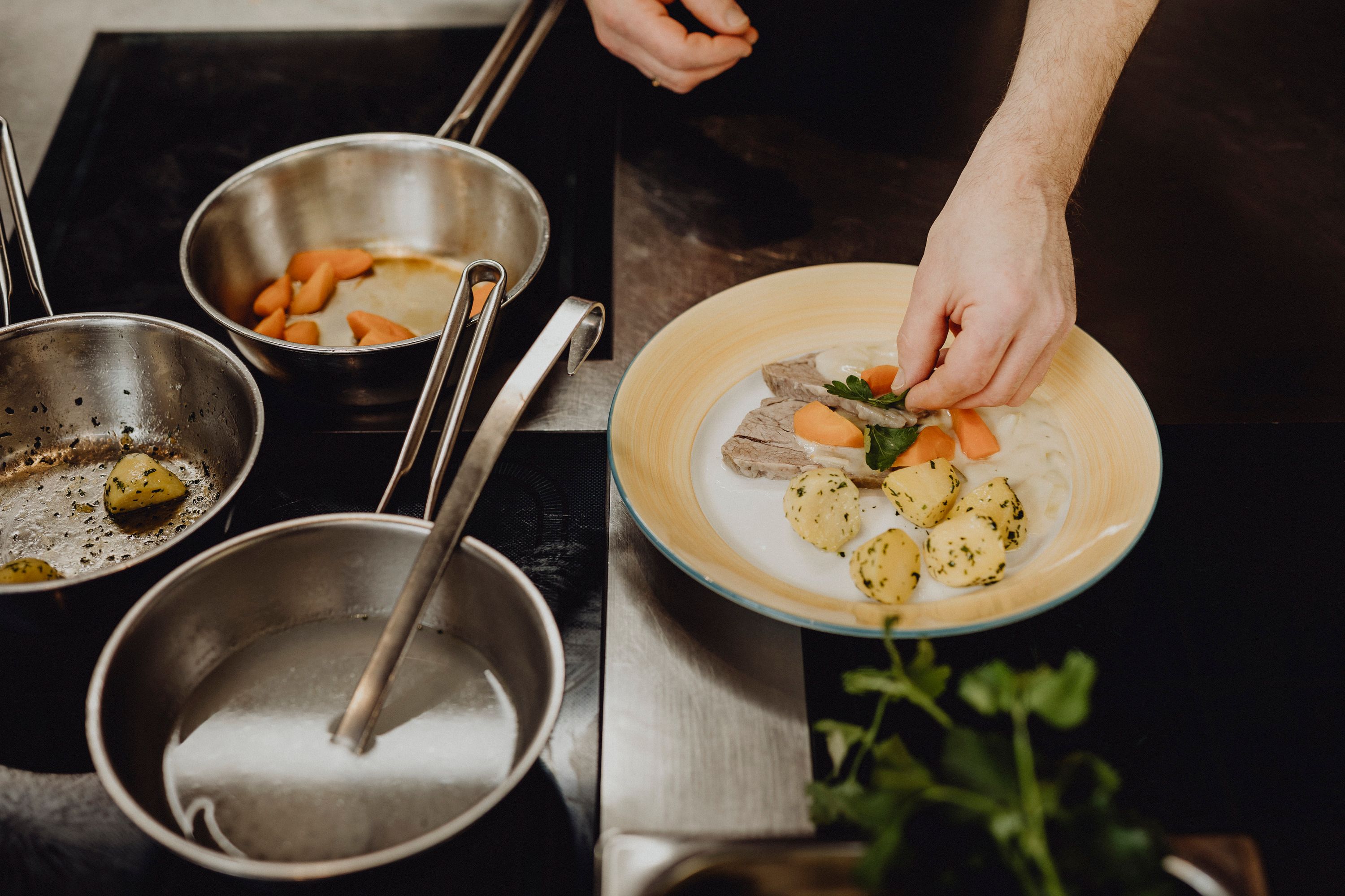 Ein Teller mit gekochtem Rindfleisch, Rahmgemüse und Kartoffeln wird angerichtet.