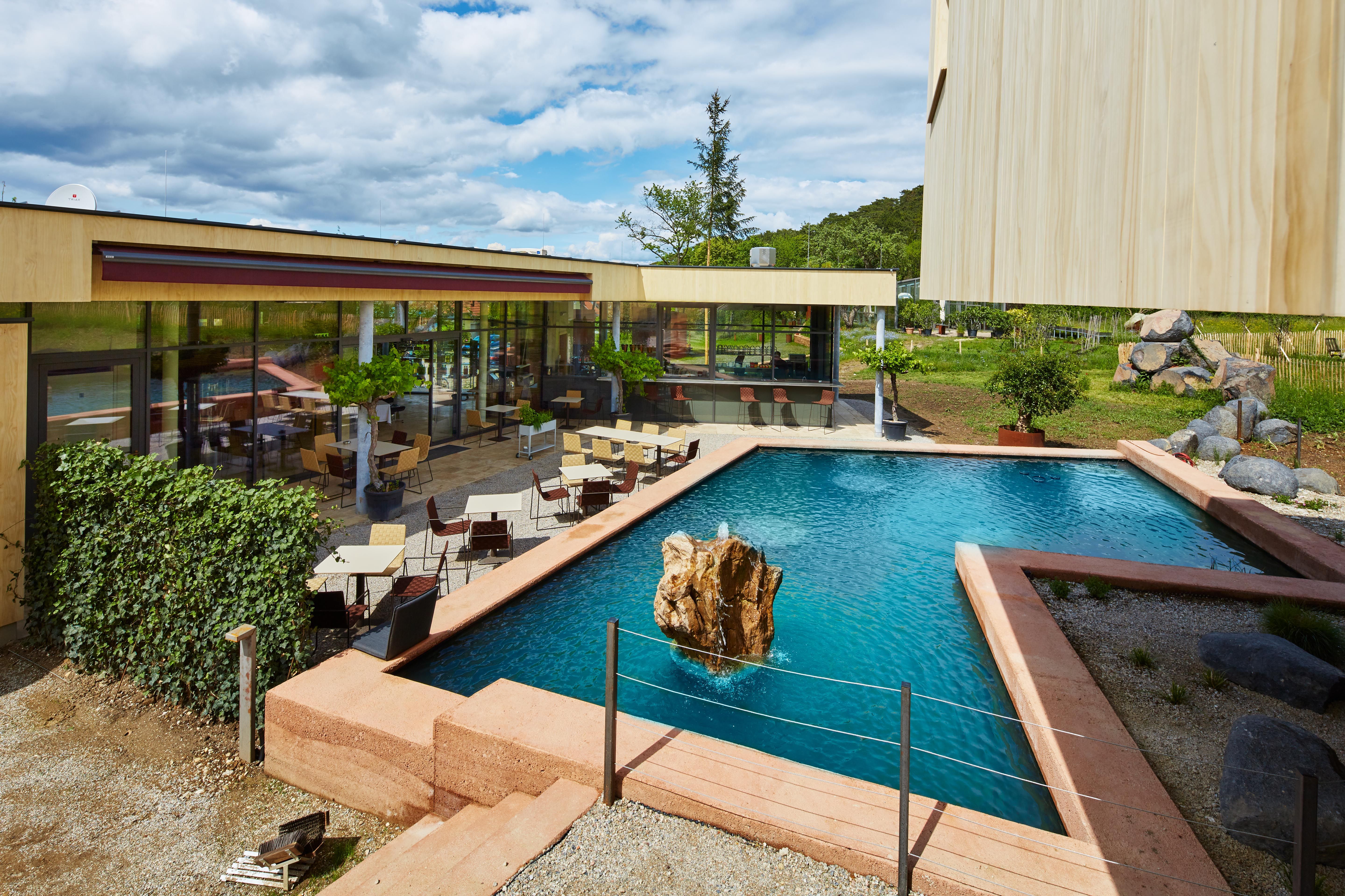 Moderne Terrasse mit Tischen und Stühlen neben einem rechteckigen Teich mit Felsen in der Mitte.