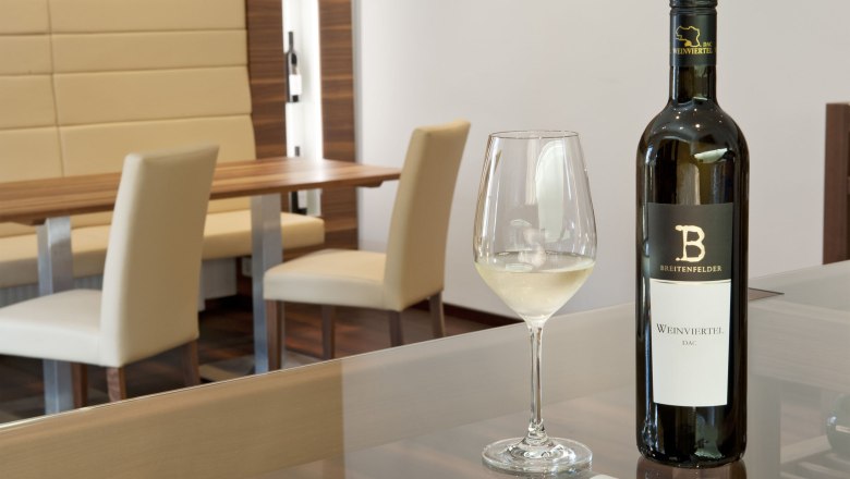 Ein Verkostungsraum mit einer Flasche Wei&szlig;wein und einem gef&uuml;llten Weinglas auf einem Tisch.