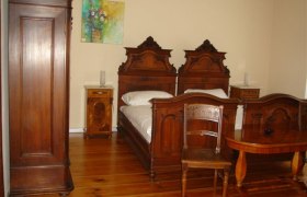 Ein traditionell eingerichtetes Schlafzimmer mit antiken Holzmöbeln, darunter zwei Betten, ein Schrank und ein Tisch.