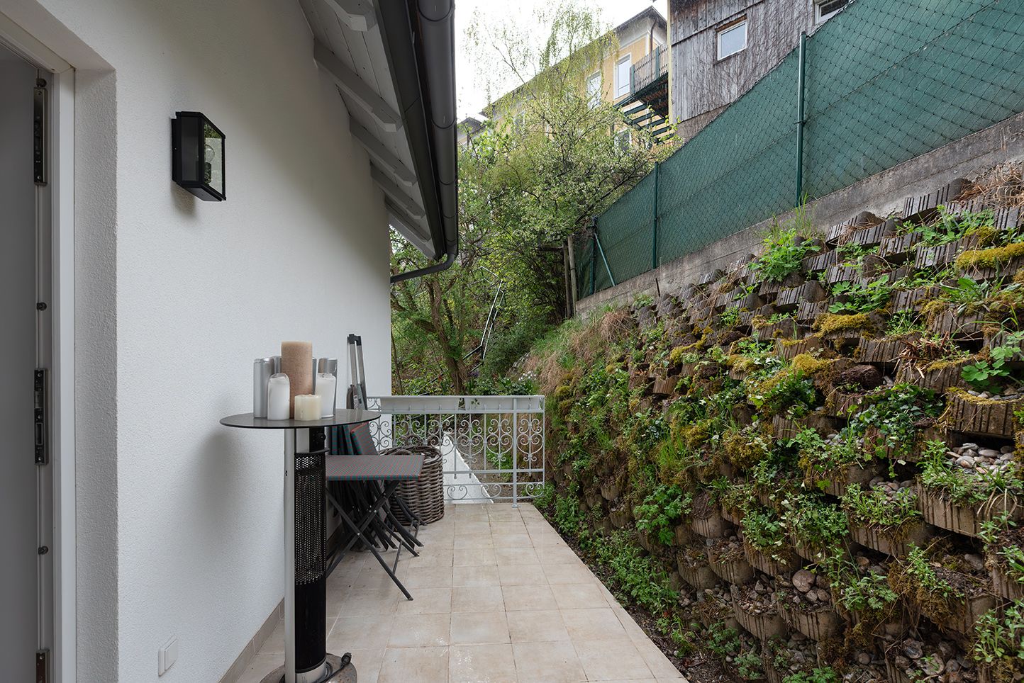 Eine Terrasse mit Tisch und Kerzen, daneben eine bepflanzte Mauer.