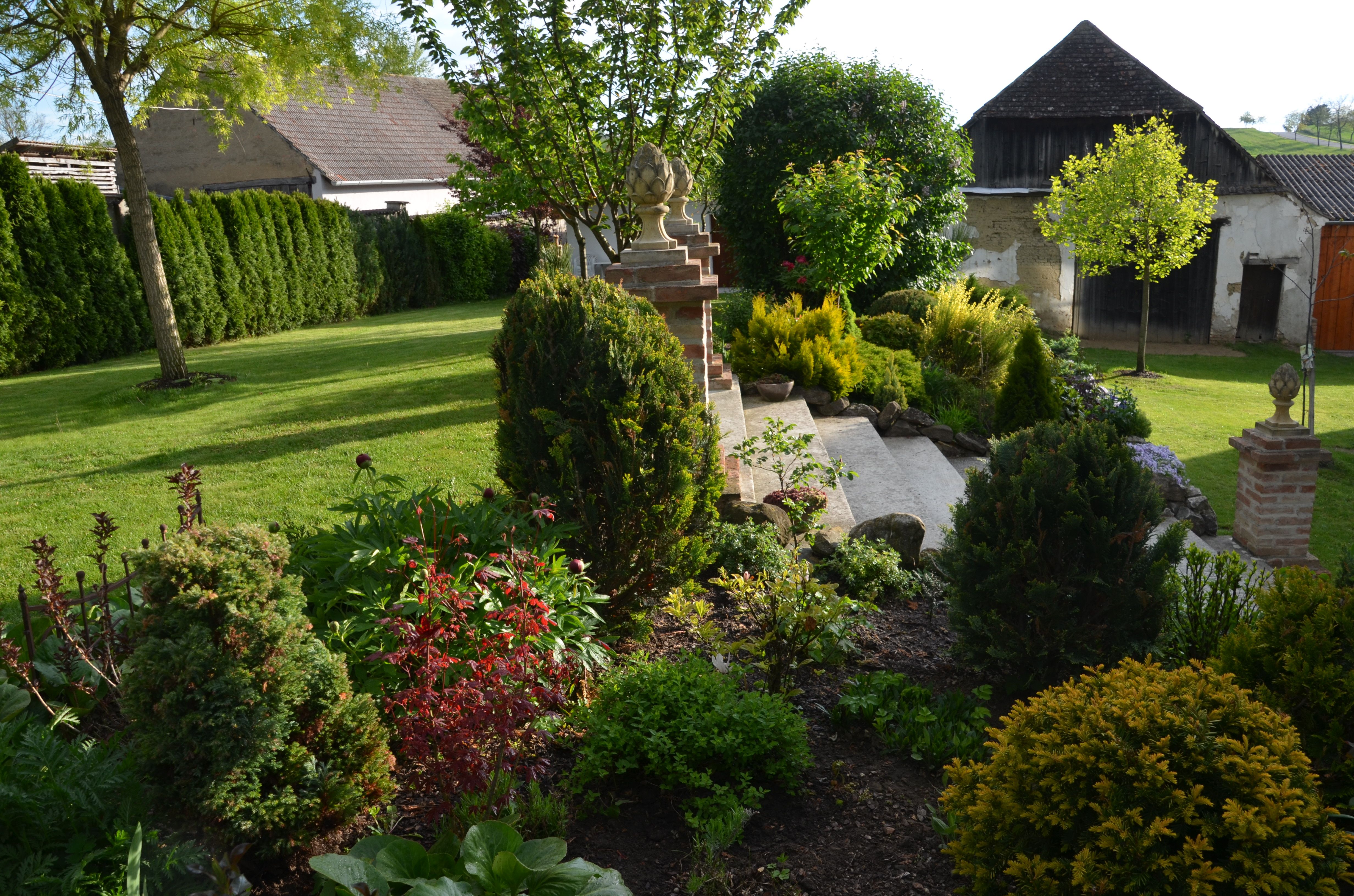 Ein gepflegter Garten mit Rasen, Büschen und Bäumen, umgeben von Gebäuden im Hintergrund.