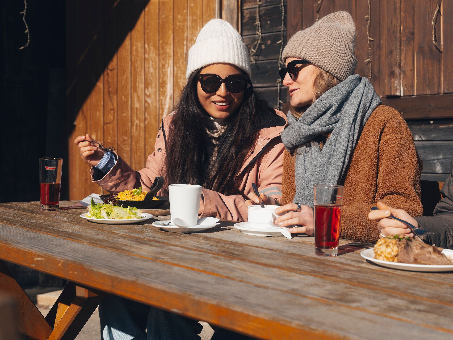 In der winterlichen Idylle genießen Freunde eine entspannte Zeit bei köstlichen Speisen und warmen Getränken. Die schneebedeckten Berge im Hintergrund schaffen eine malerische Kulisse, die zum Verweilen einlädt. Hier wird die Gemütlichkeit der Wiener Alpen in vollen Zügen erlebt.