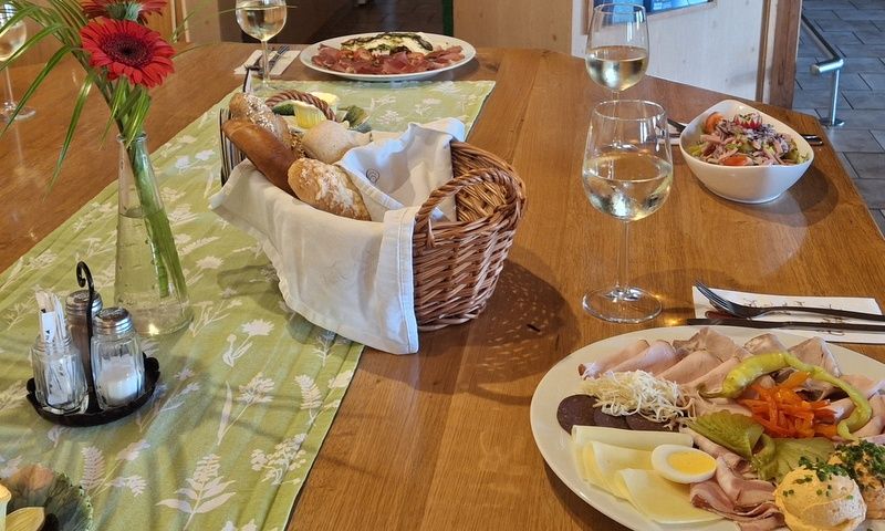 Ein gedeckter Tisch mit Wurst- und Käseplatte, Brotkorb, Salat und Weingläsern.