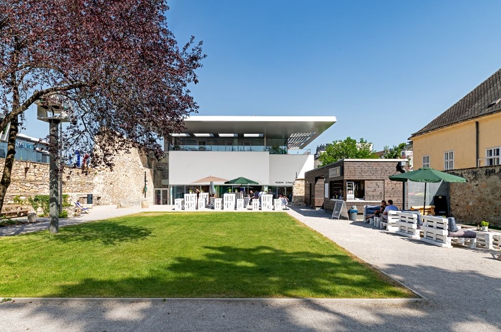 Moderner Garten mit Rasenfläche, Sitzbereich und Gebäuden im Hintergrund.