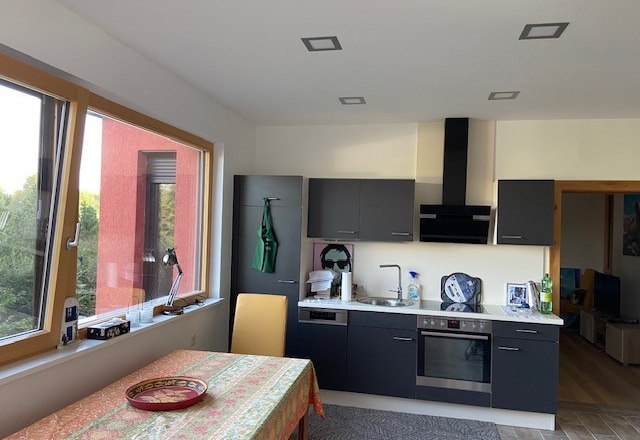 Moderne Küche mit grauen Schränken, Herd, Spüle und Tisch mit bunter Tischdecke.