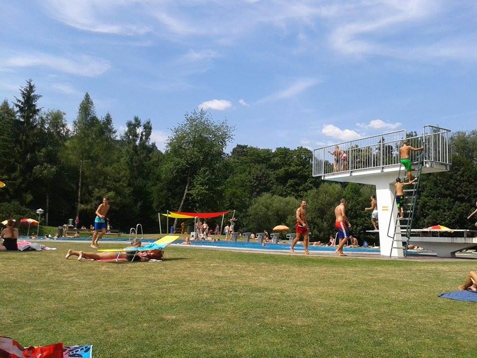 Menschen im Parkbad Seebenstein, einige auf der Wiese, andere im Pool. Ein Sprungturm ist zu sehen.