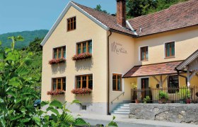 Außenansicht eines gelben Gästehauses mit roten Dachziegeln und Blumenkästen an den Fenstern.