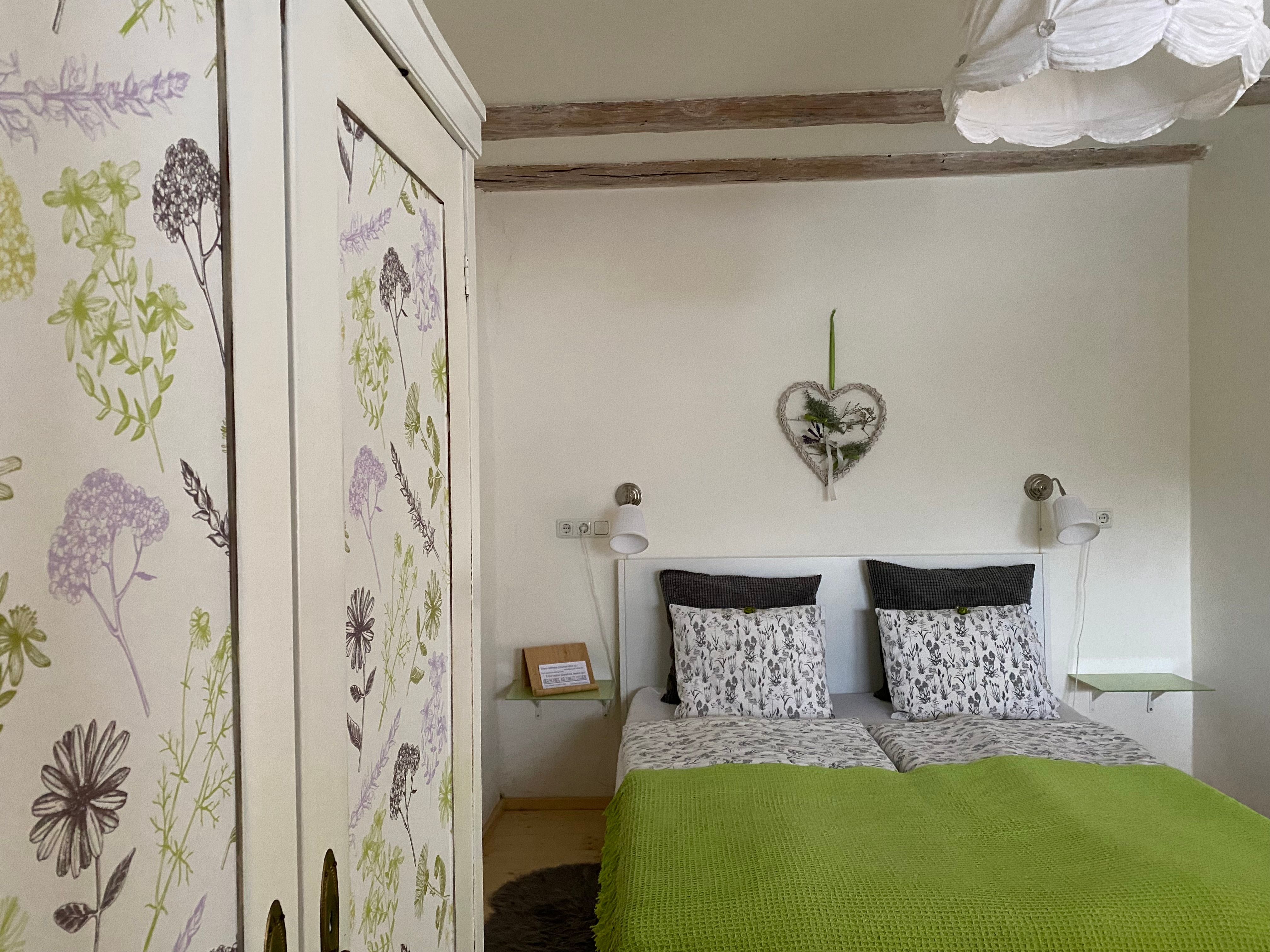 Gemütliches Doppelzimmer mit floralem Kleiderschrank und grüner Bettdecke.