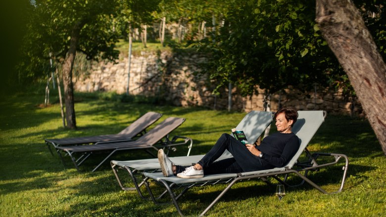 Person liest auf einer Sonnenliege im Garten.