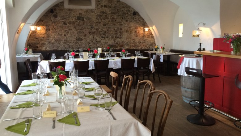 Gemütlicher Gastraum mit gedeckten Tischen, Steinwand und gewölbter Decke.