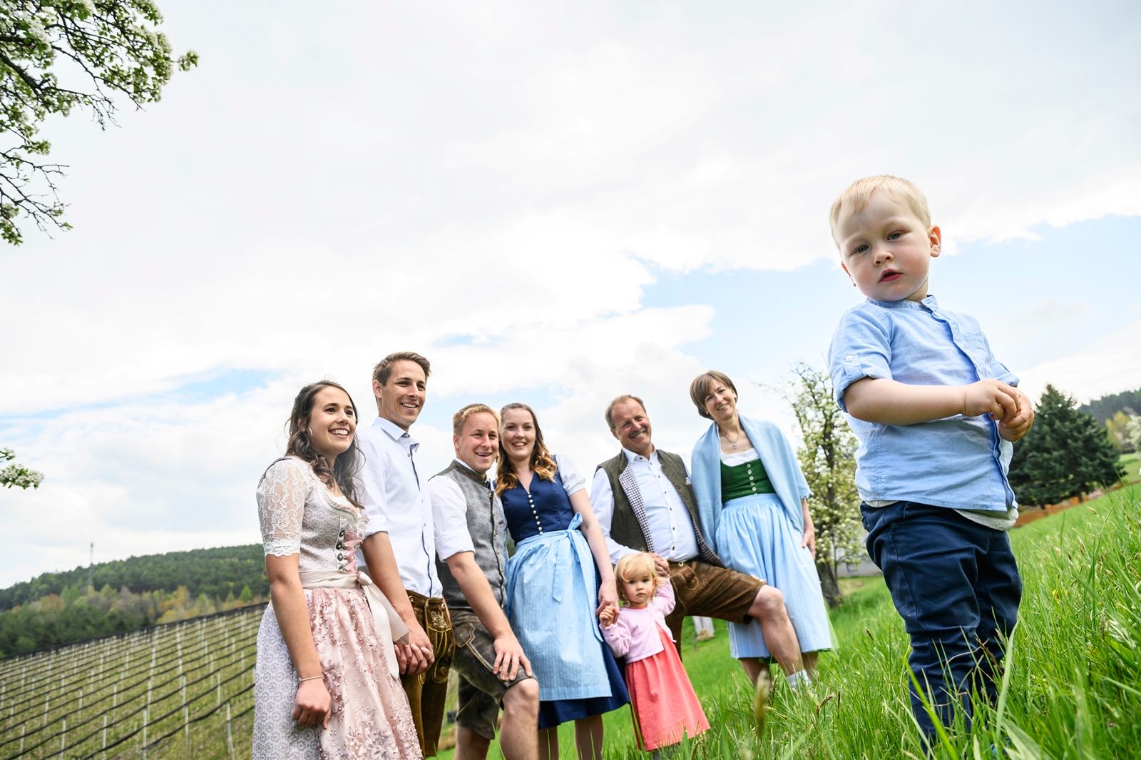 Eine Familie in traditioneller Kleidung steht auf einer Wiese, ein kleiner Junge im Vordergrund.