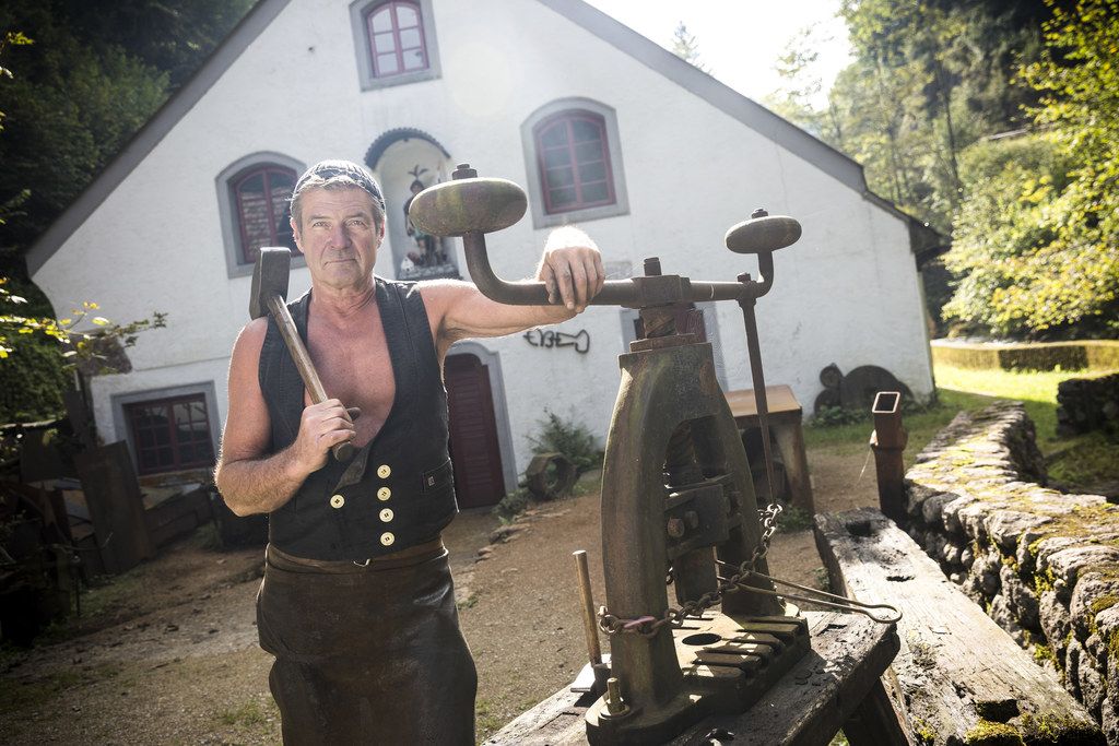 Ein Mann in traditioneller Kleidung steht vor einem historischen Gebäude mit Werkzeugen.