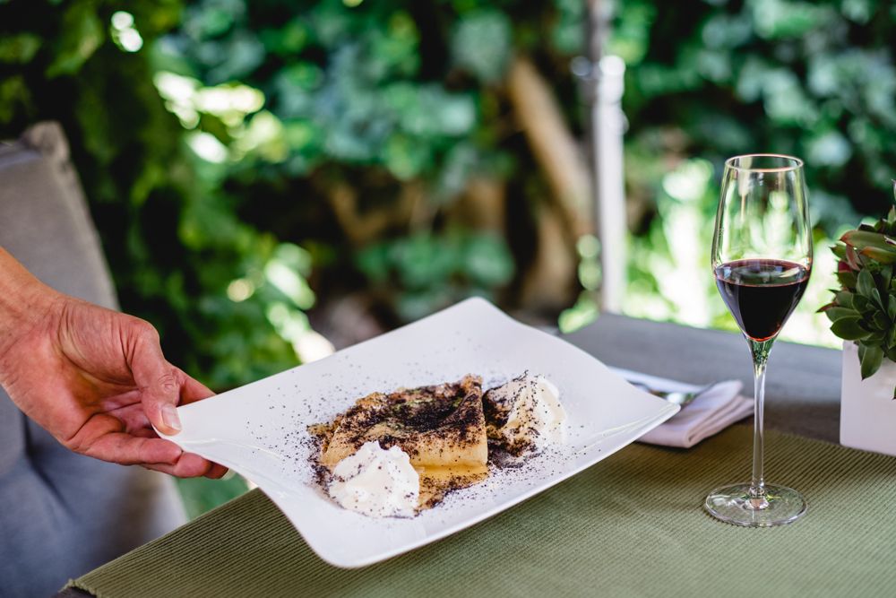 Dessert mit Mohn und Sahne auf Teller, Glas Rotwein daneben.