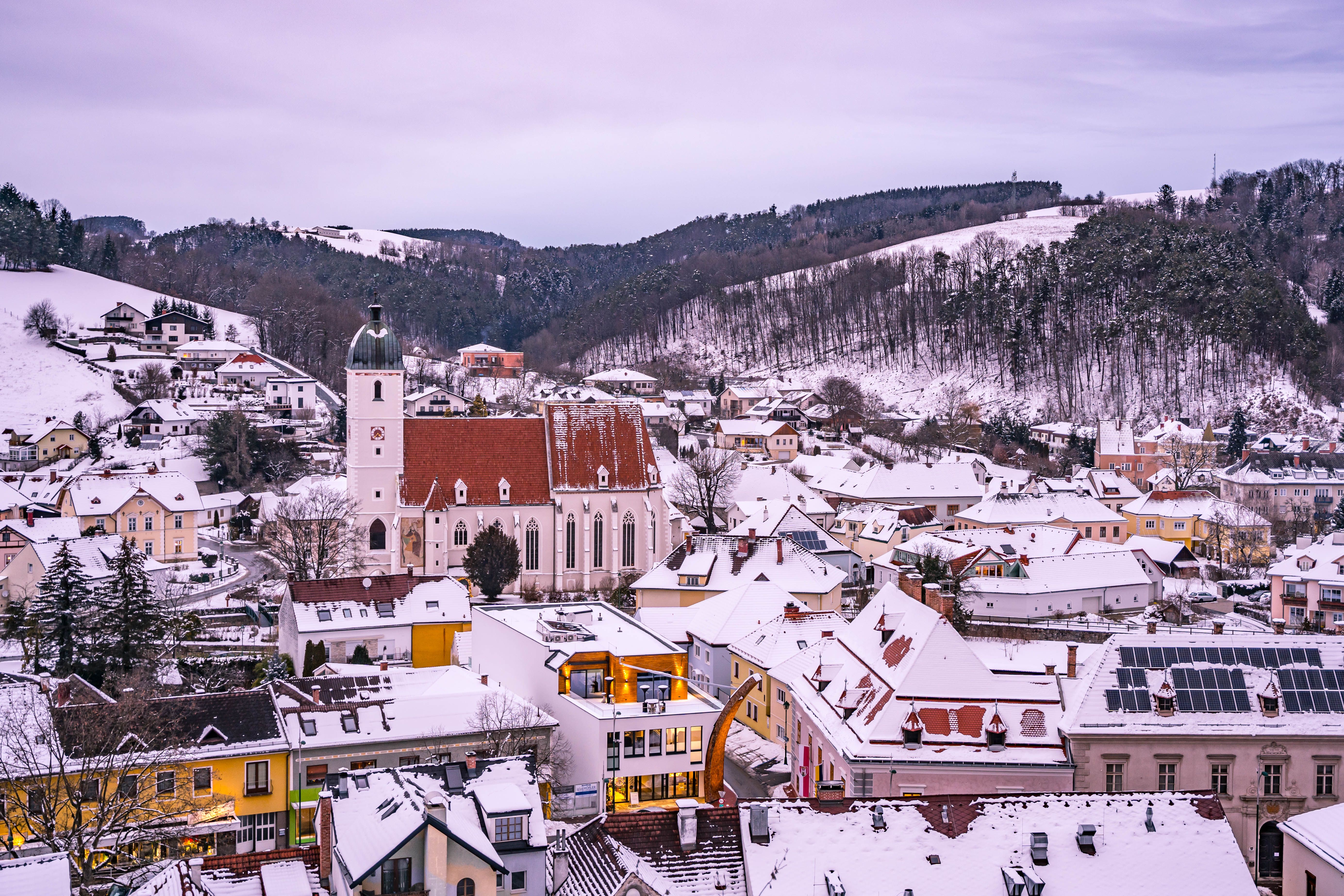Winterliche Stadtansicht von Kirchschlag mit schneebedeckten Dächern und einer Kirche im Vordergrund.