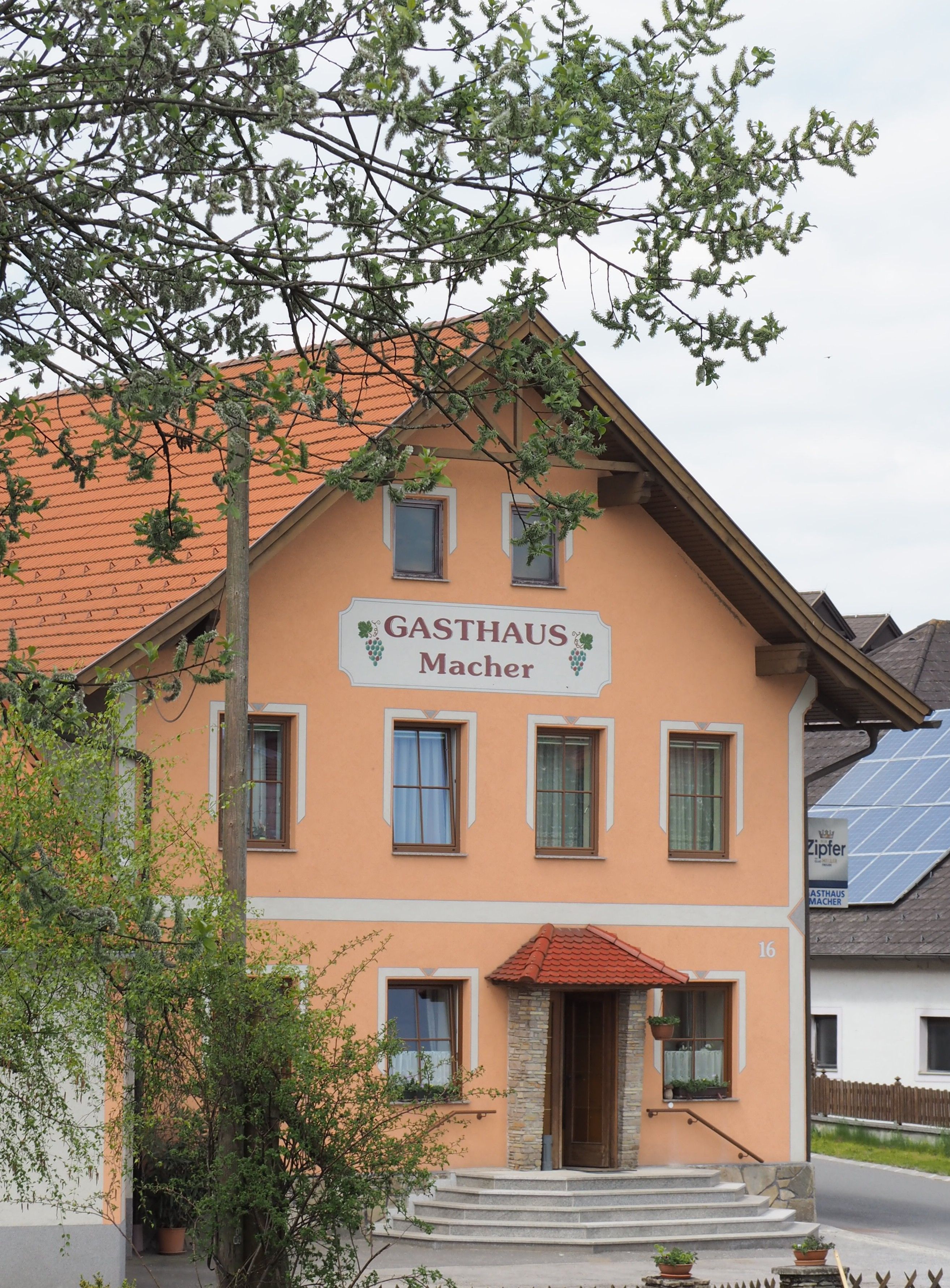 Ein traditionelles Gasthaus mit orangefarbener Fassade und roten Dachziegeln, umgeben von Bäumen.