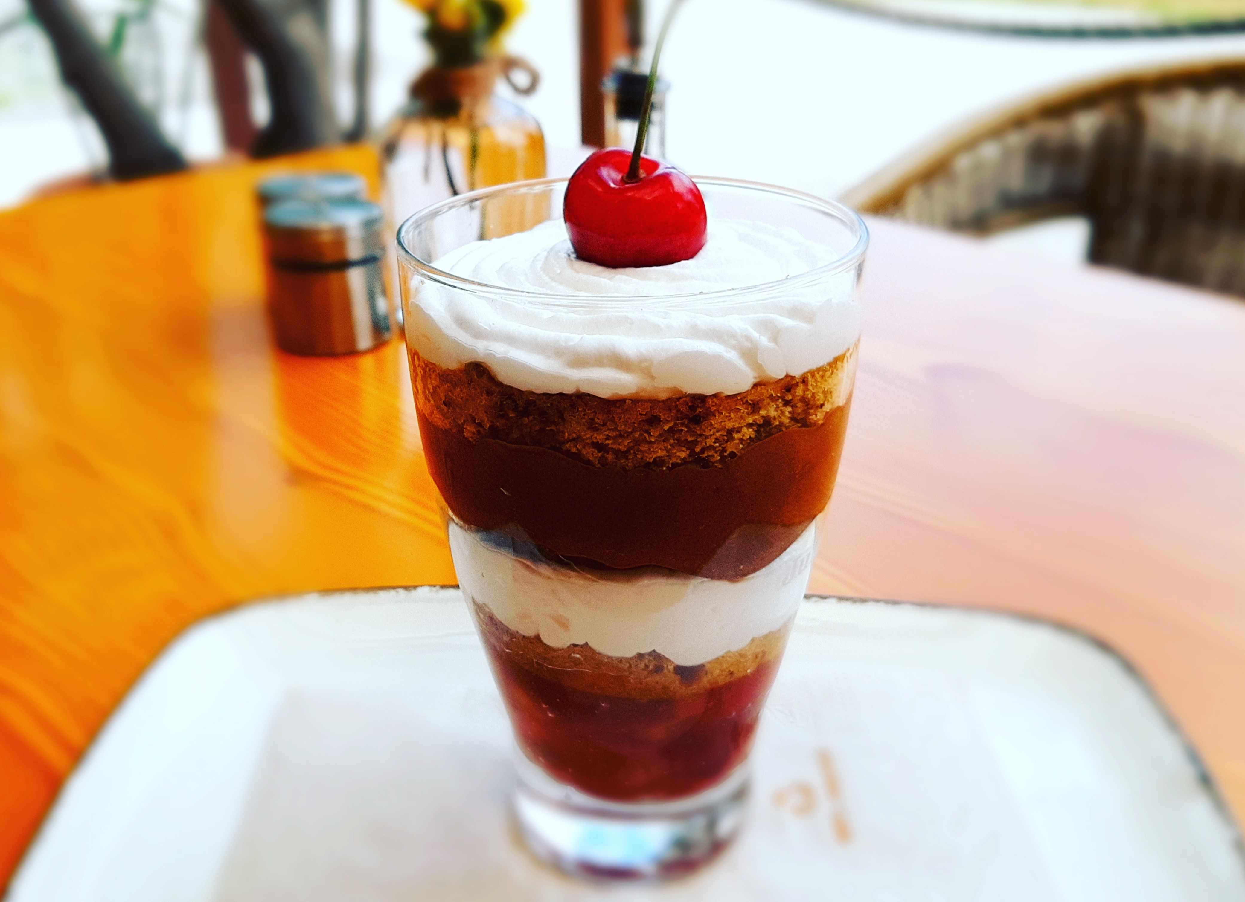 Ein Dessert im Glas mit Schichten aus Sahne, Kuchen und Kirschen, garniert mit einer Kirsche.