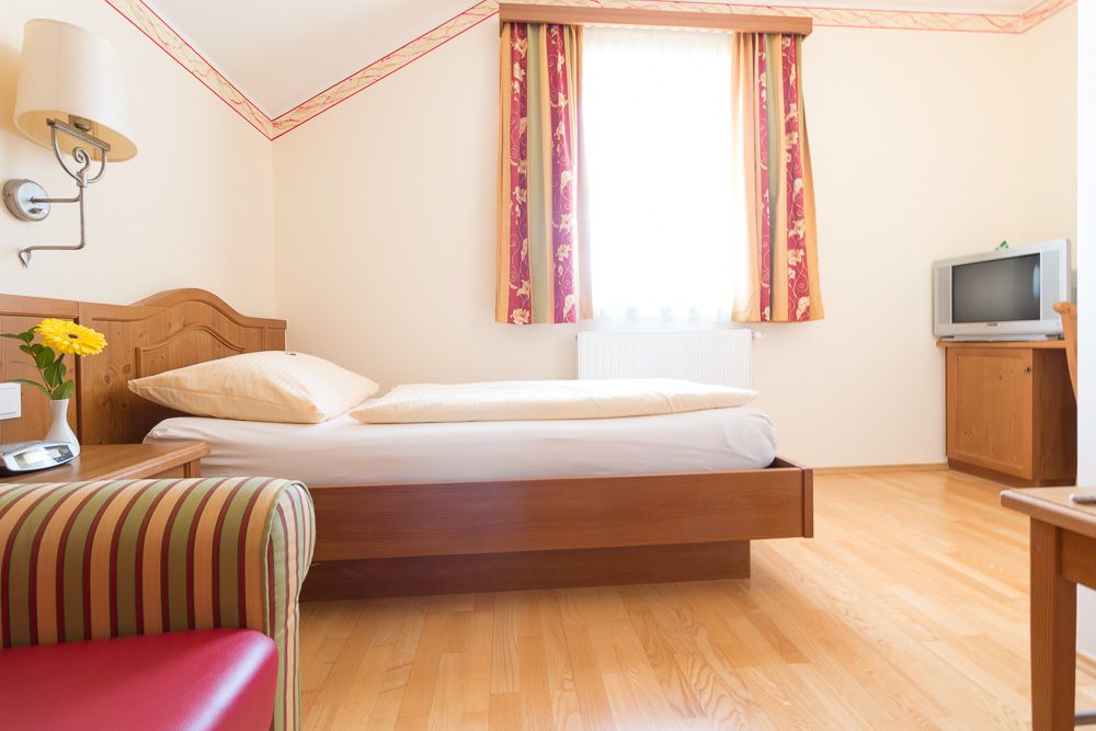 Einzelzimmer mit Bett, Fernseher und Sessel.