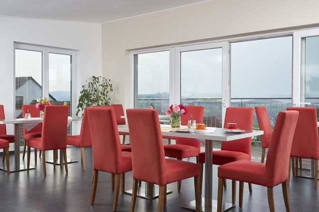 Frühstücksraum mit roten Stühlen, Holzmöbeln und Kaffeemaschine.