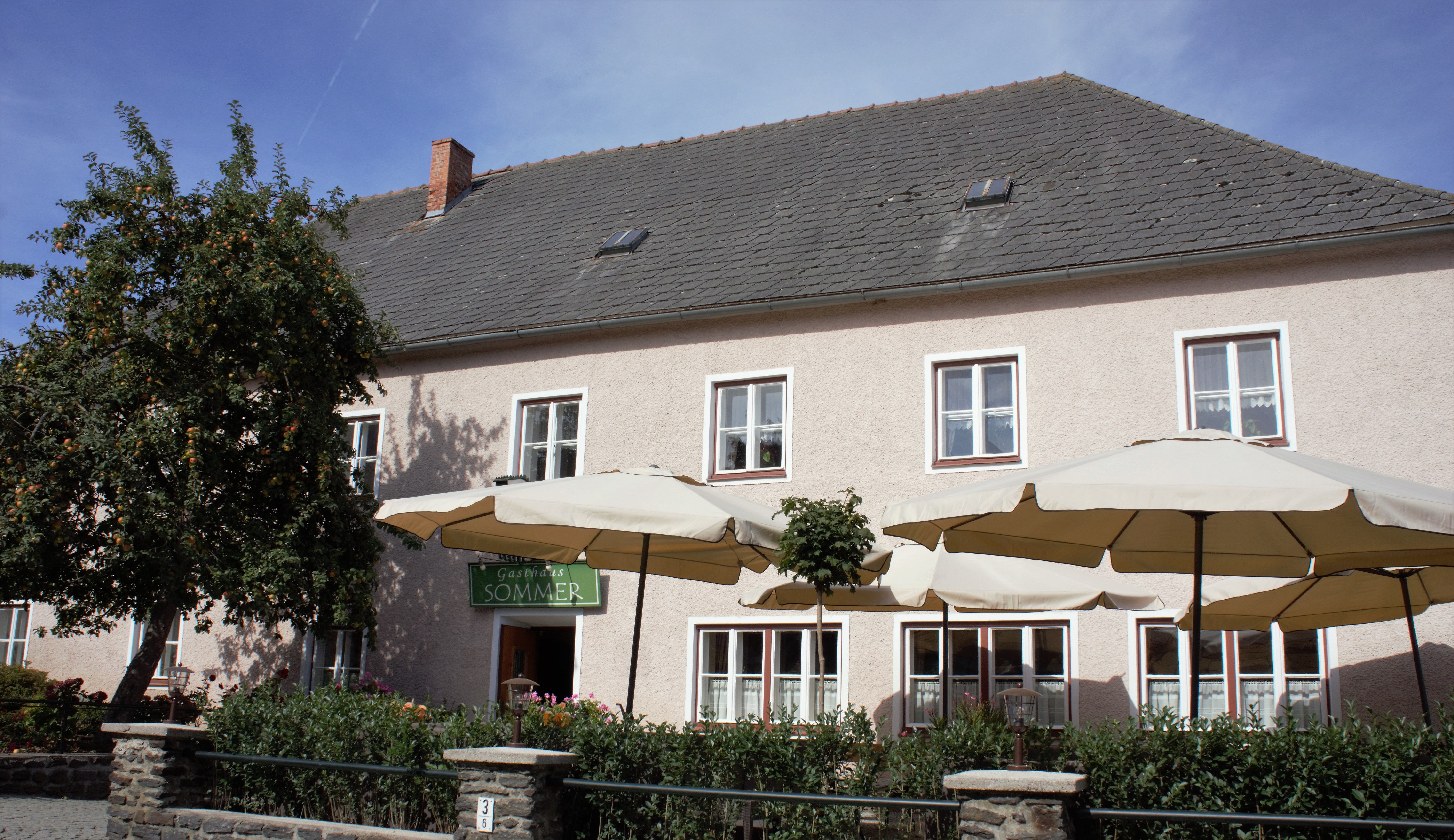 Ein traditionelles Gasthaus mit Sonnenschirmen und einem Baum im Vordergrund.